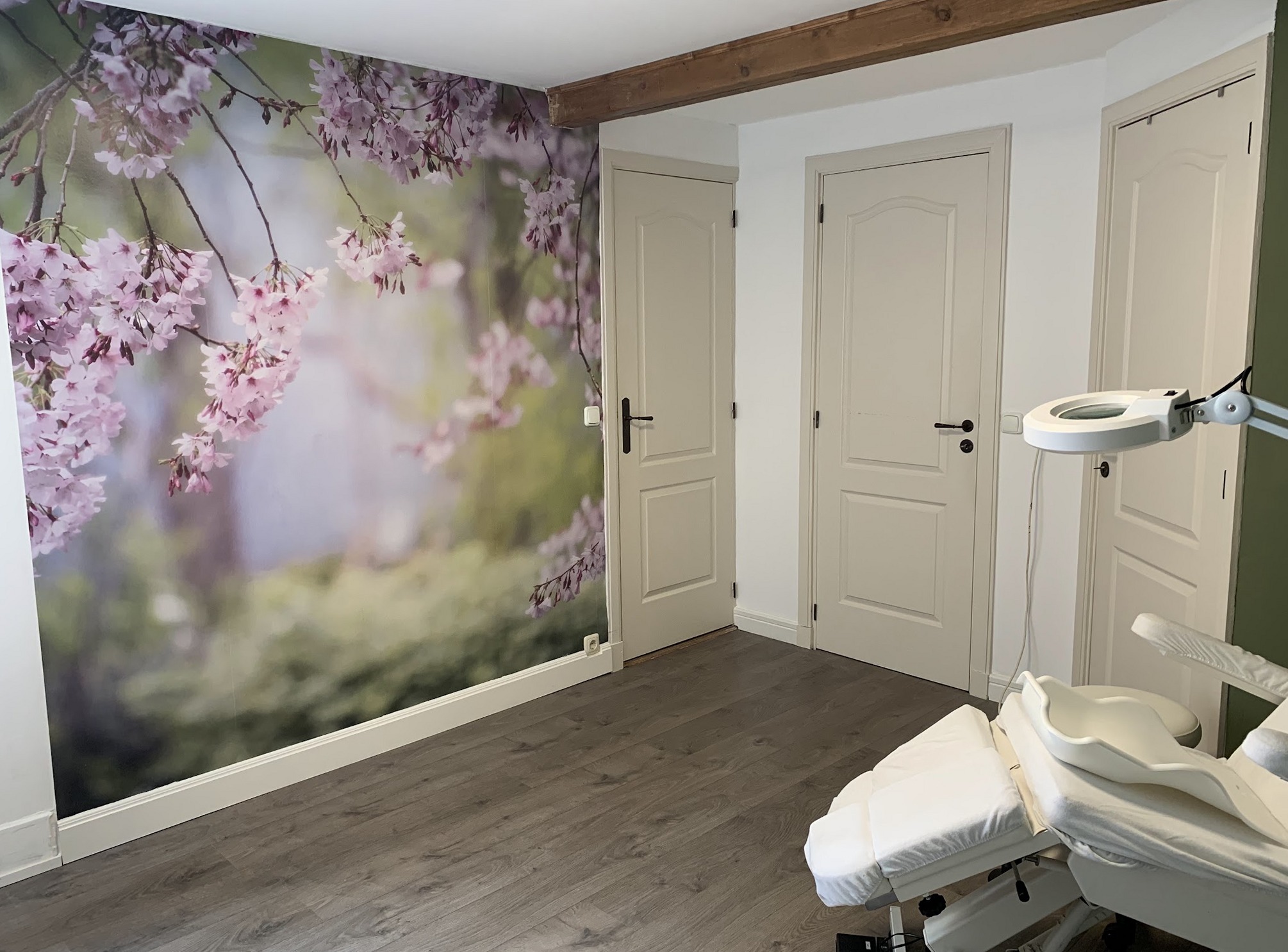 De behandelruimte van Pedicure Tammerijn: een wand met kersenbloesem, witte deuren en de behandelstoel met looplamp