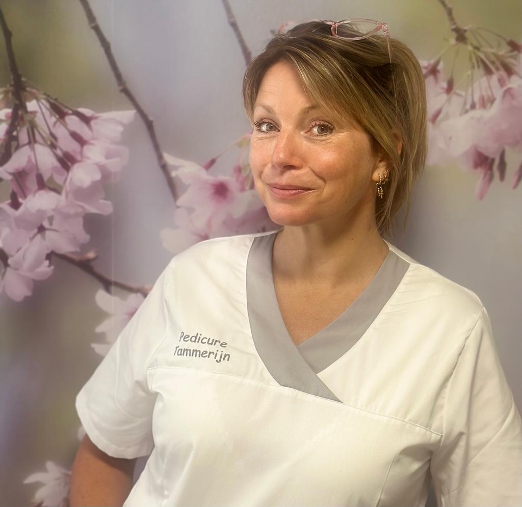 Inge Tammerijn in haar witte tuniek met Pedicure Tammerijn erop geborduurd, voor de bloesemwand in haar praktijk